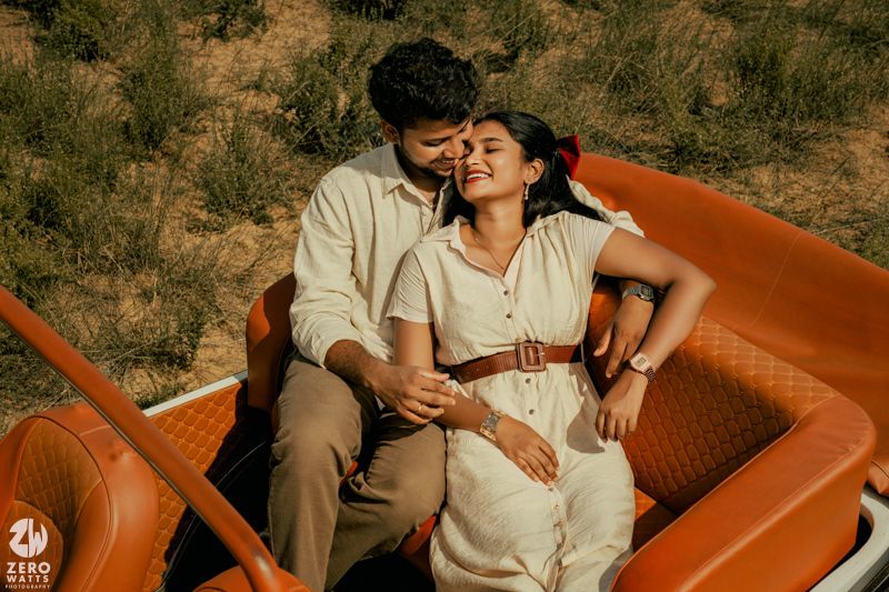 Couple relaxing in the front seats of an orange vintage convertible car.