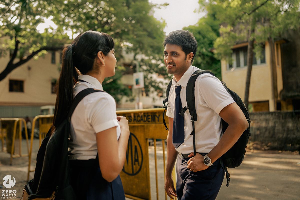 Students gathered in conversation along a sunlit school corridor with brick walls.