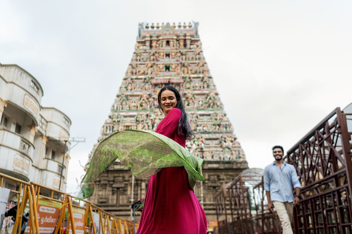 Traditional dancers perform in front of ornate temple architecture with white gopurams and detailed carvings in the background.