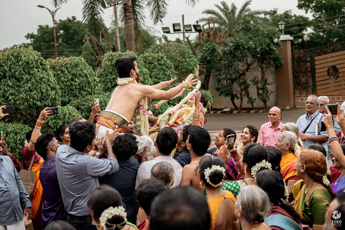 Guests gather excitedly outdoors under palm trees during a festive celebration.
