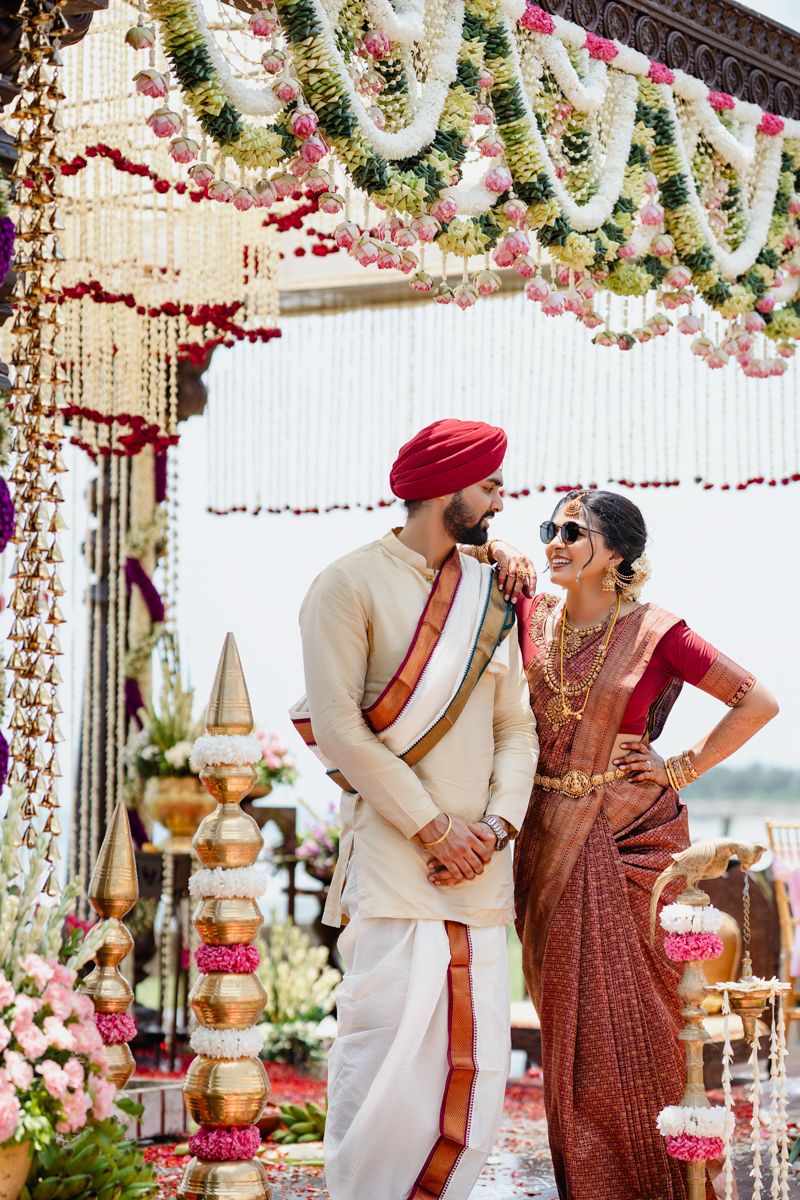 Outdoor Indian wedding ceremony under floral mandap with pink and white hanging decorations.