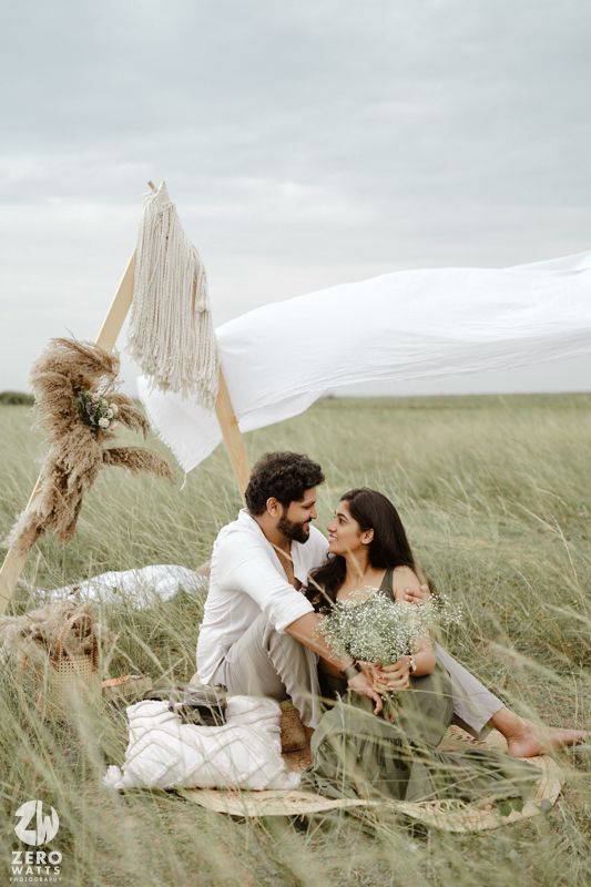 Romantic outdoor photoshoot with pampas grass decorations in a grassy field under cloudy skies.