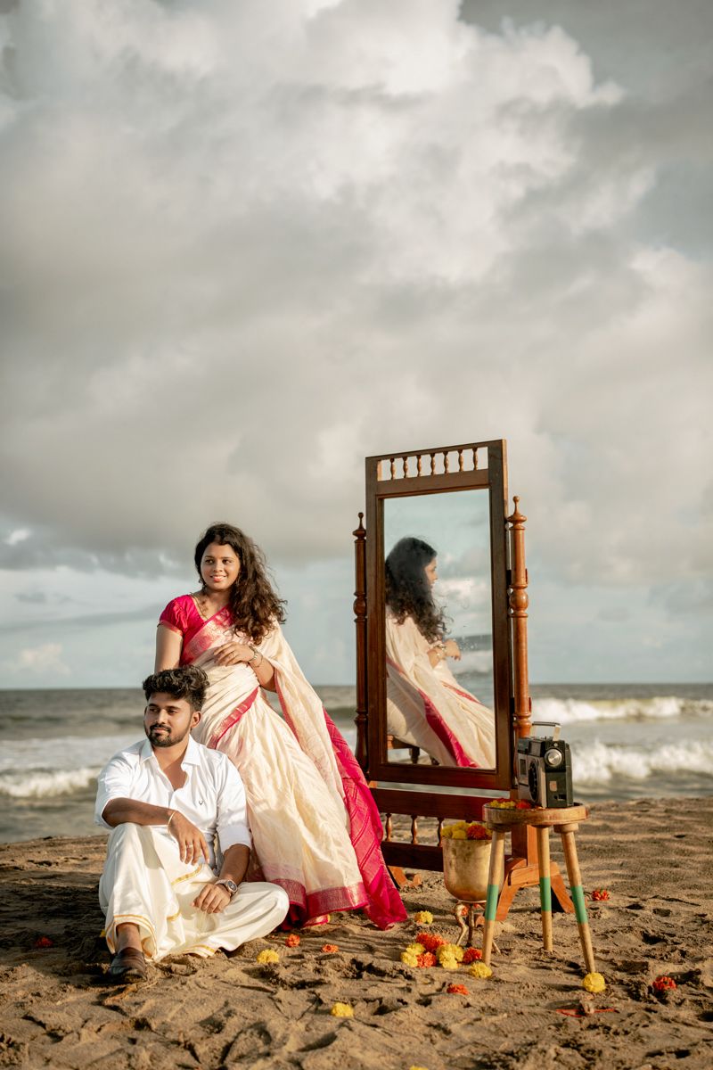 Romantic beach photoshoot setup with vintage wooden mirror and decorative elements on sandy shore at sunset.