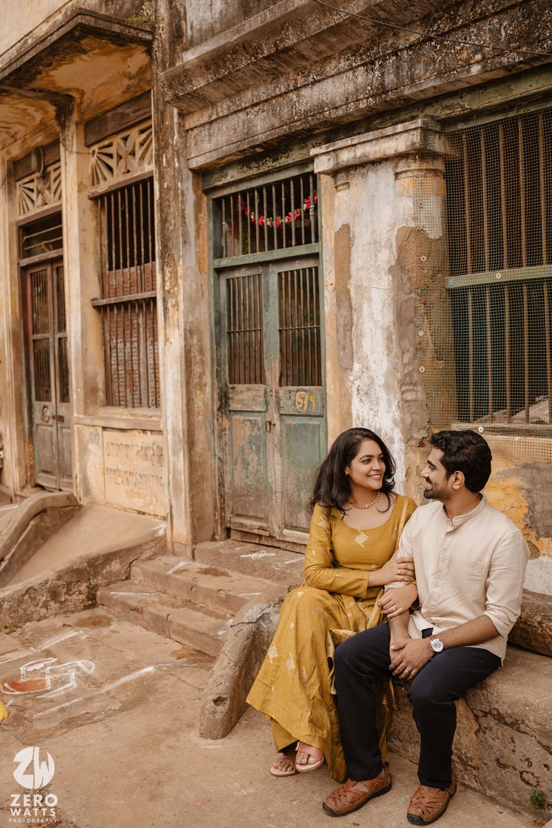 Couple shares intimate moments while sitting against weathered walls in vintage architectural setting.