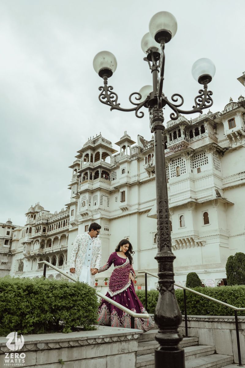 Couple in traditional Indian attire pose on steps of ornate City Palace in Udaipur with vintage lamp post.