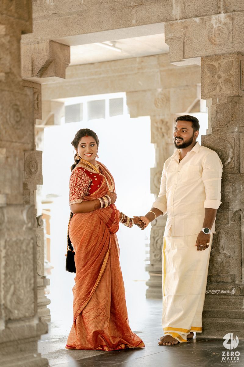 Couple in traditional Indian attire sharing romantic moments in a sunlit temple corridor with stone pillars.