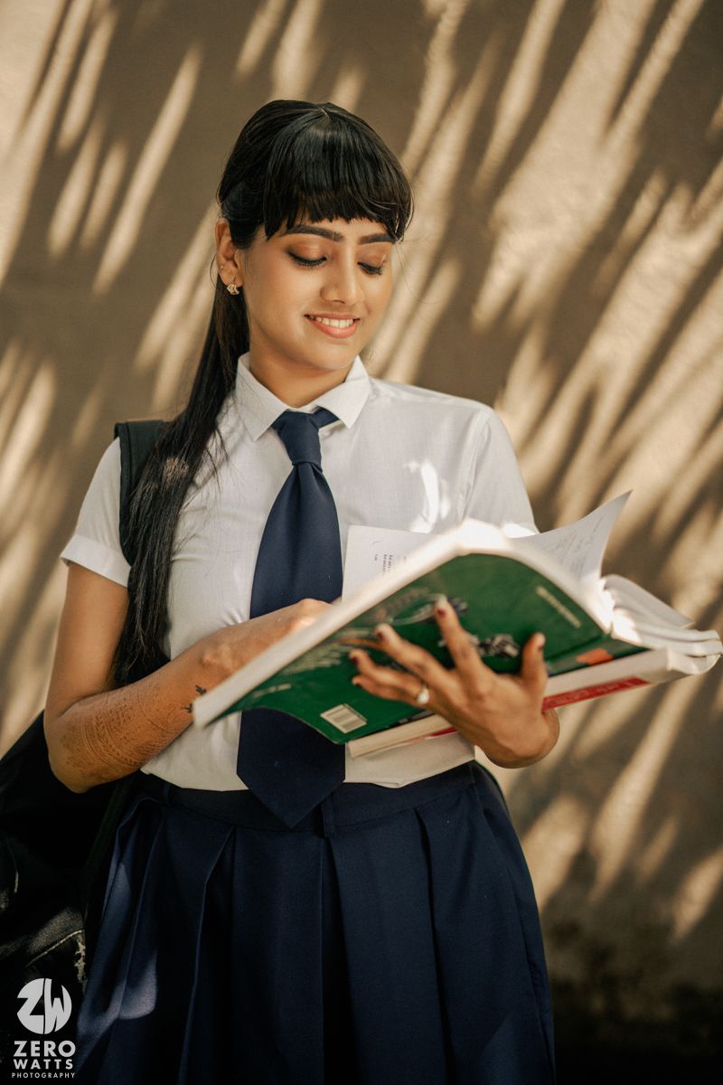 Student in school uniform reading a textbook against a wall with dramatic shadow patterns.