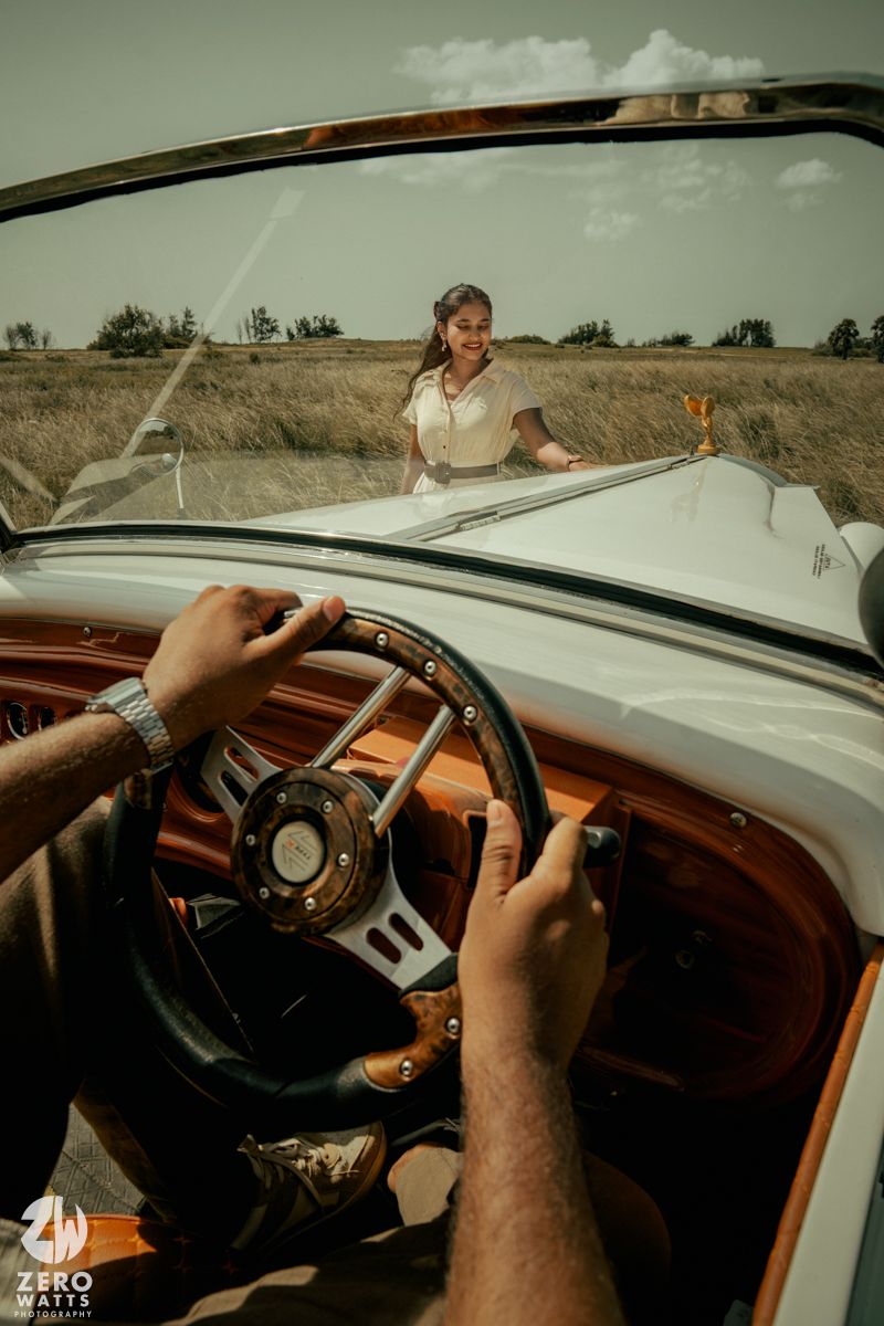First-person view from driver's seat of classic car with wooden dashboard and steering wheel in countryside.