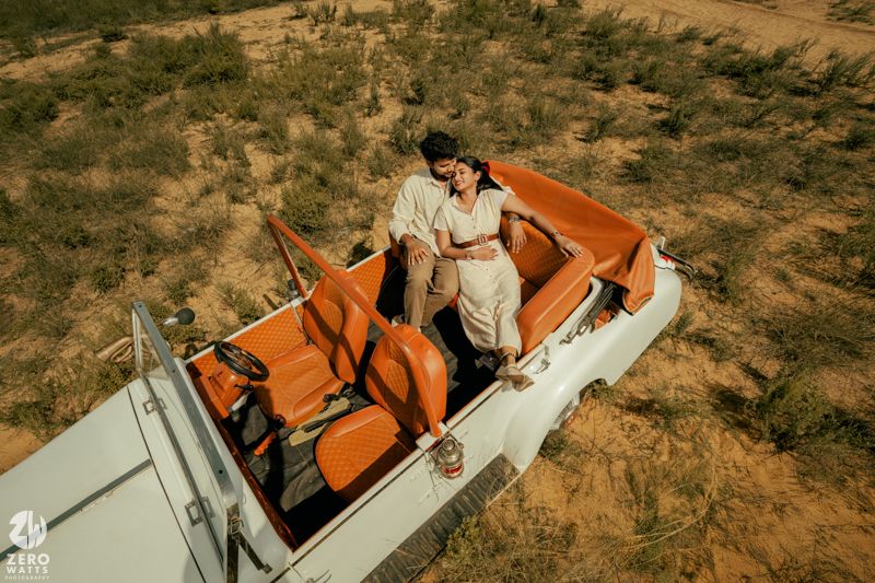 Panoramic view of a vintage orange and white car parked in a desert landscape.