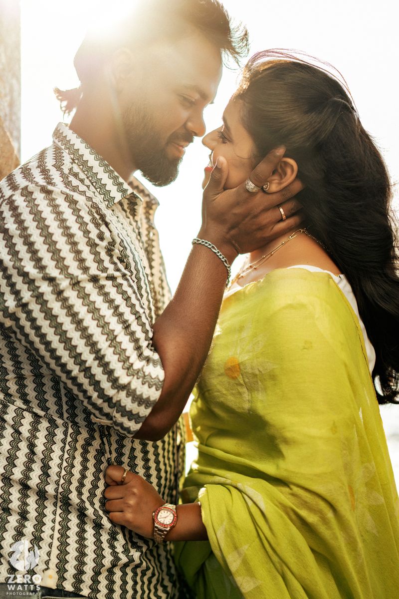 A backlit couple embraces tenderly in front of a bright sunlit background.
