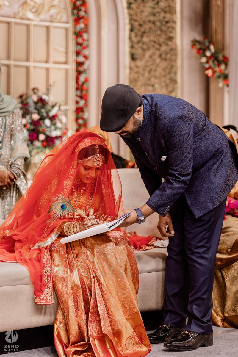 A traditional Indian wedding ceremony shows a bride in red attire signing documents during the marriage ritual.
