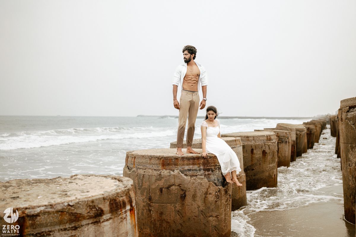 Couple posing on weathered stone sea breakers with ocean waves in the background on an overcast day.