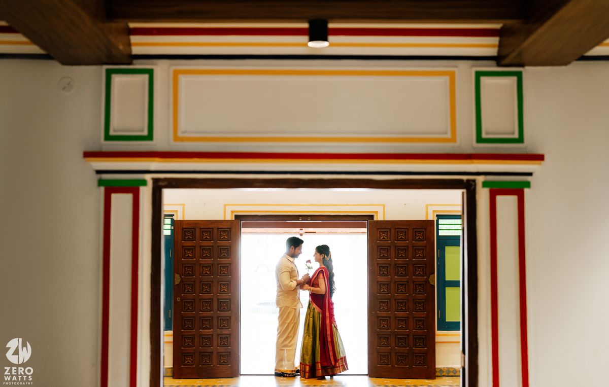 South Indian couple standing in a beautifully framed traditional doorway with colorful painted borders.