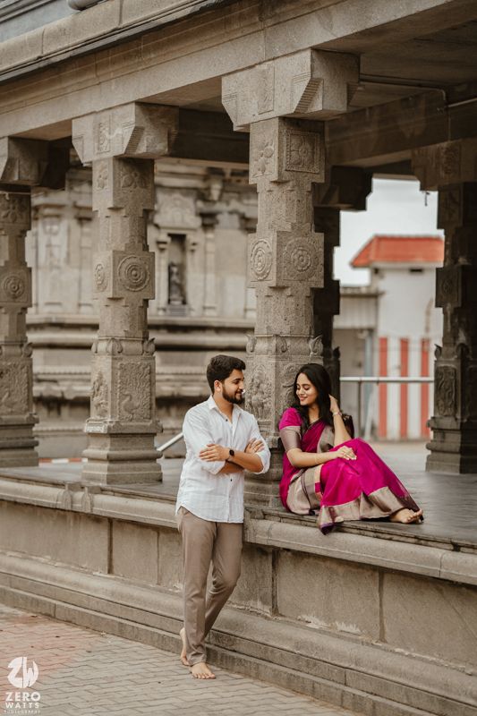A couple shares romantic moments in a traditional stone corridor with ornate pillars and architectural details.