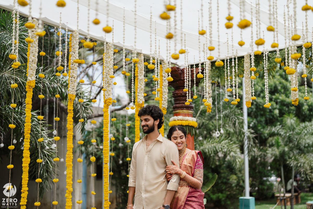 Outdoor wedding venue decorated with hanging yellow marigold garlands and string lights.