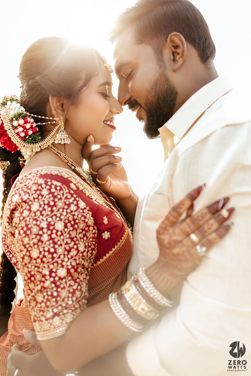 A couple in traditional Indian wedding attire share an intimate moment during a backlit golden hour photoshoot.