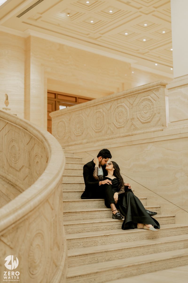 A couple shares a tender moment while sitting on curved marble stairs in an elegant interior.