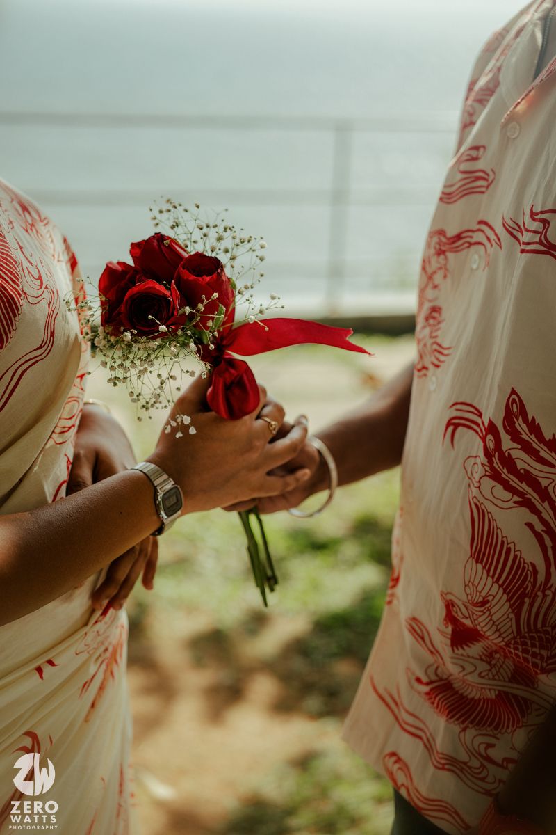 Close-up of hands holding red roses against white and red patterned clothing in natural light.