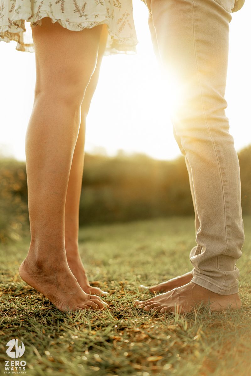 Bare feet of a couple standing close together on grass during sunset.