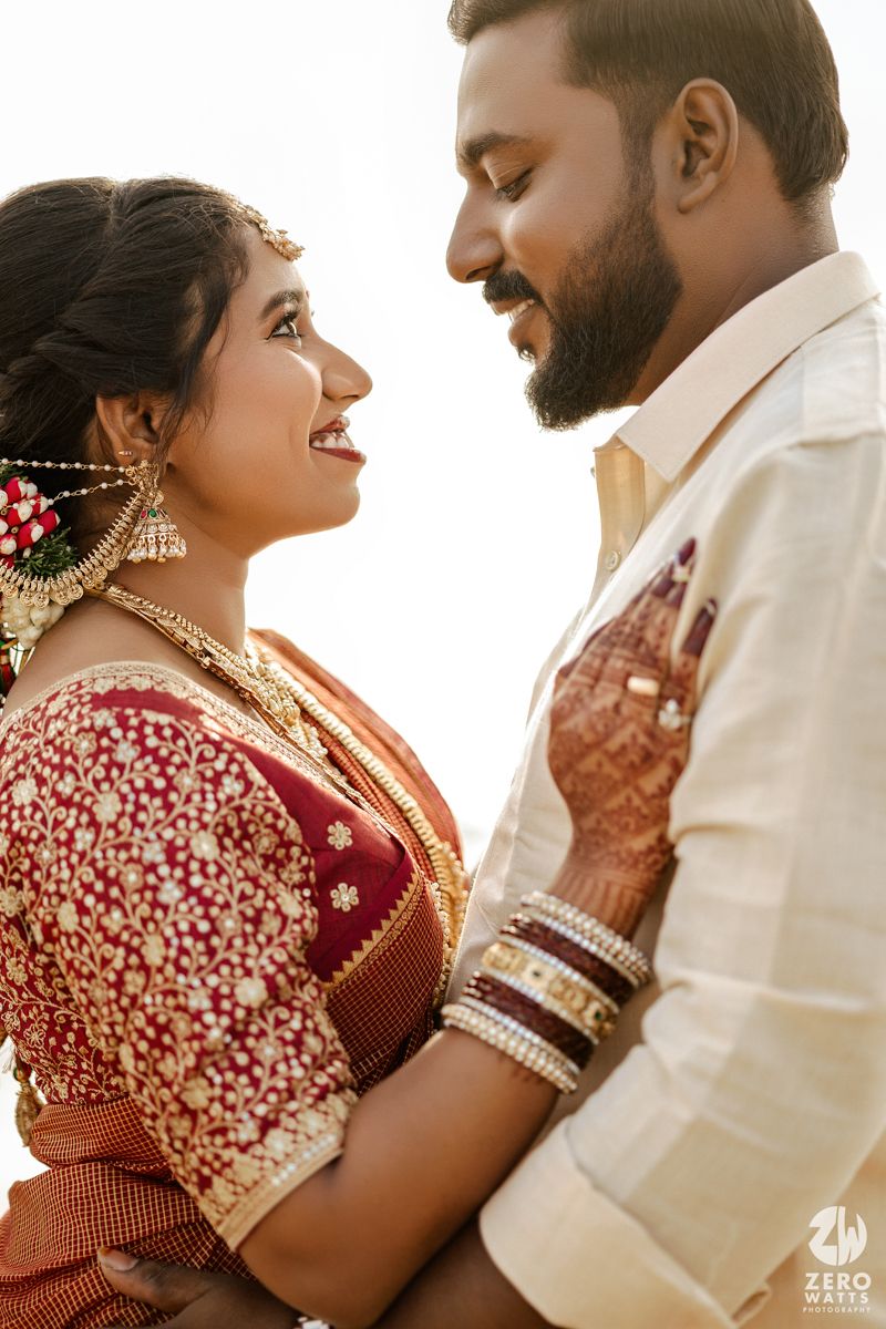 A romantic moment captured between a couple in traditional South Indian wedding attire showing joyful expressions.
