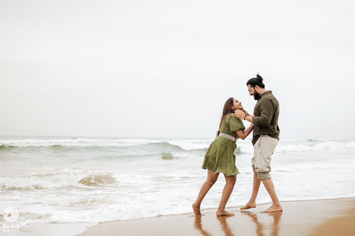 Two people playfully splash in the ocean waves at the beach on an overcast day.