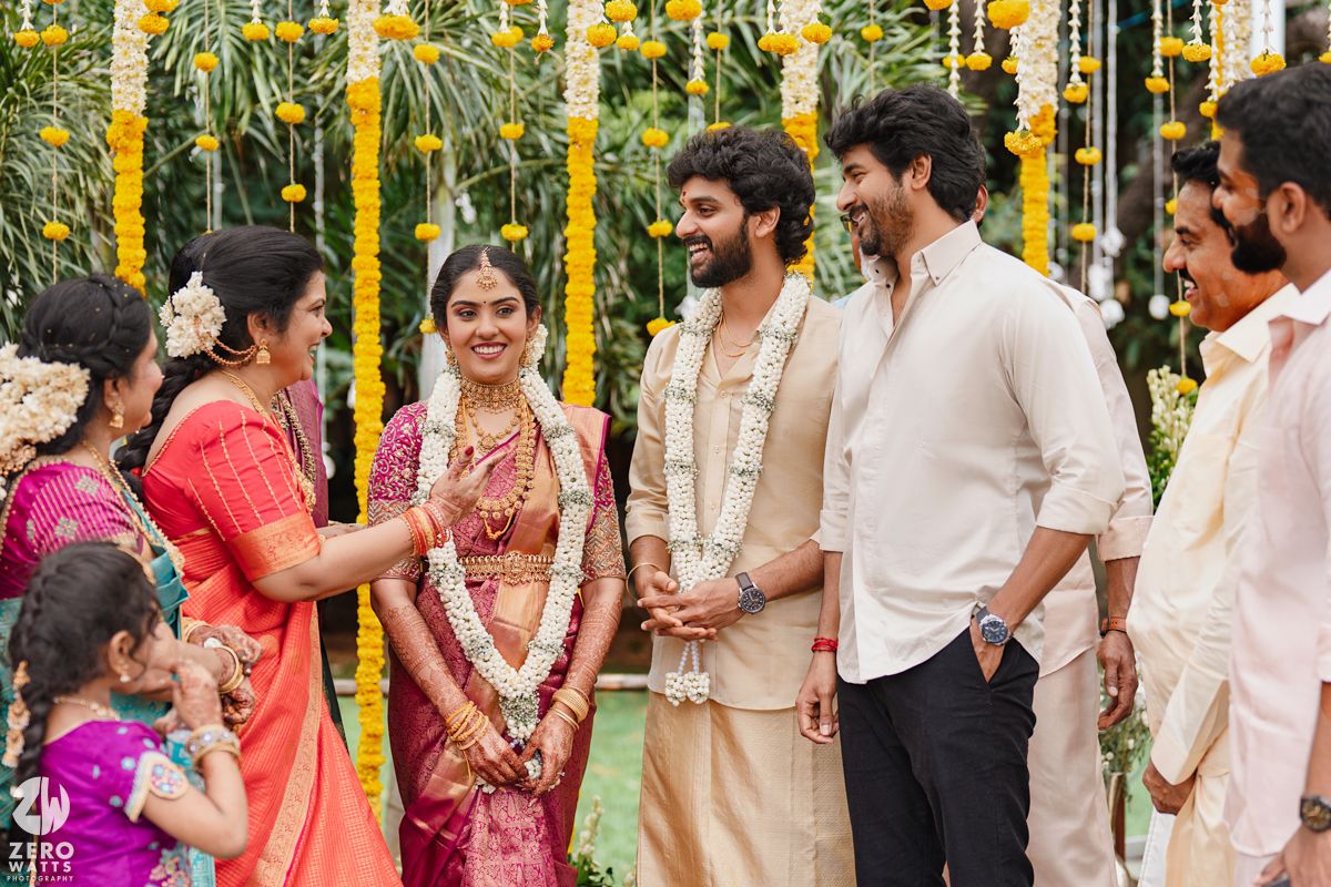 Wedding guests and couple gather under yellow floral decorations at outdoor Indian ceremony.