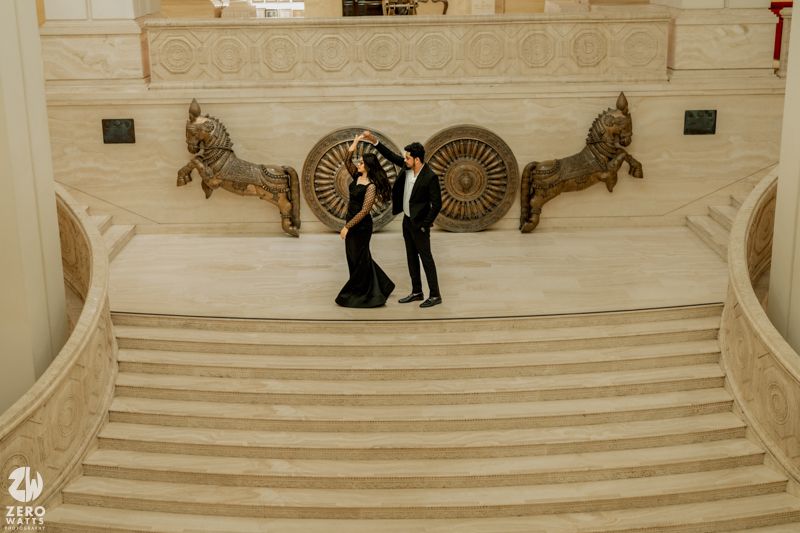 Wide view of elegant white marble staircase with ornamental details and people scattered throughout the space.