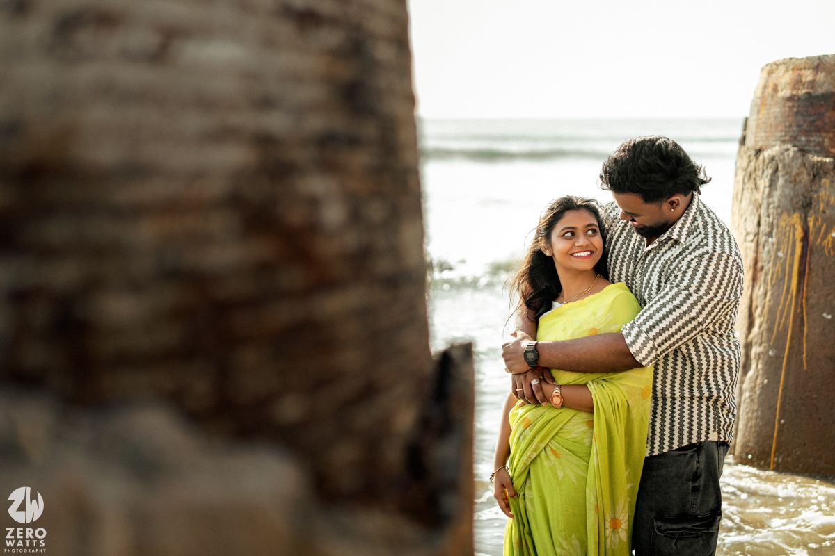 A romantic scene unfolds between two people in traditional dress by ancient stone pillars near water.