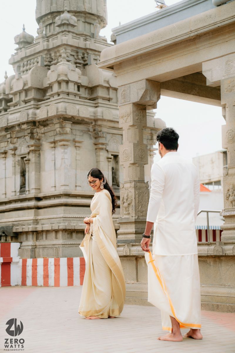 Traditional temple architecture with white-clad figures walking through stone pillared hallway.
