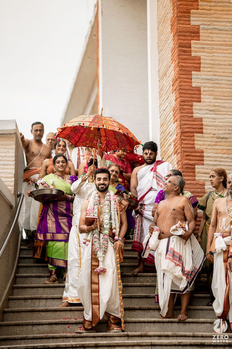 Wedding party descending stone steps with colorful parasols and traditional Indian attire.
