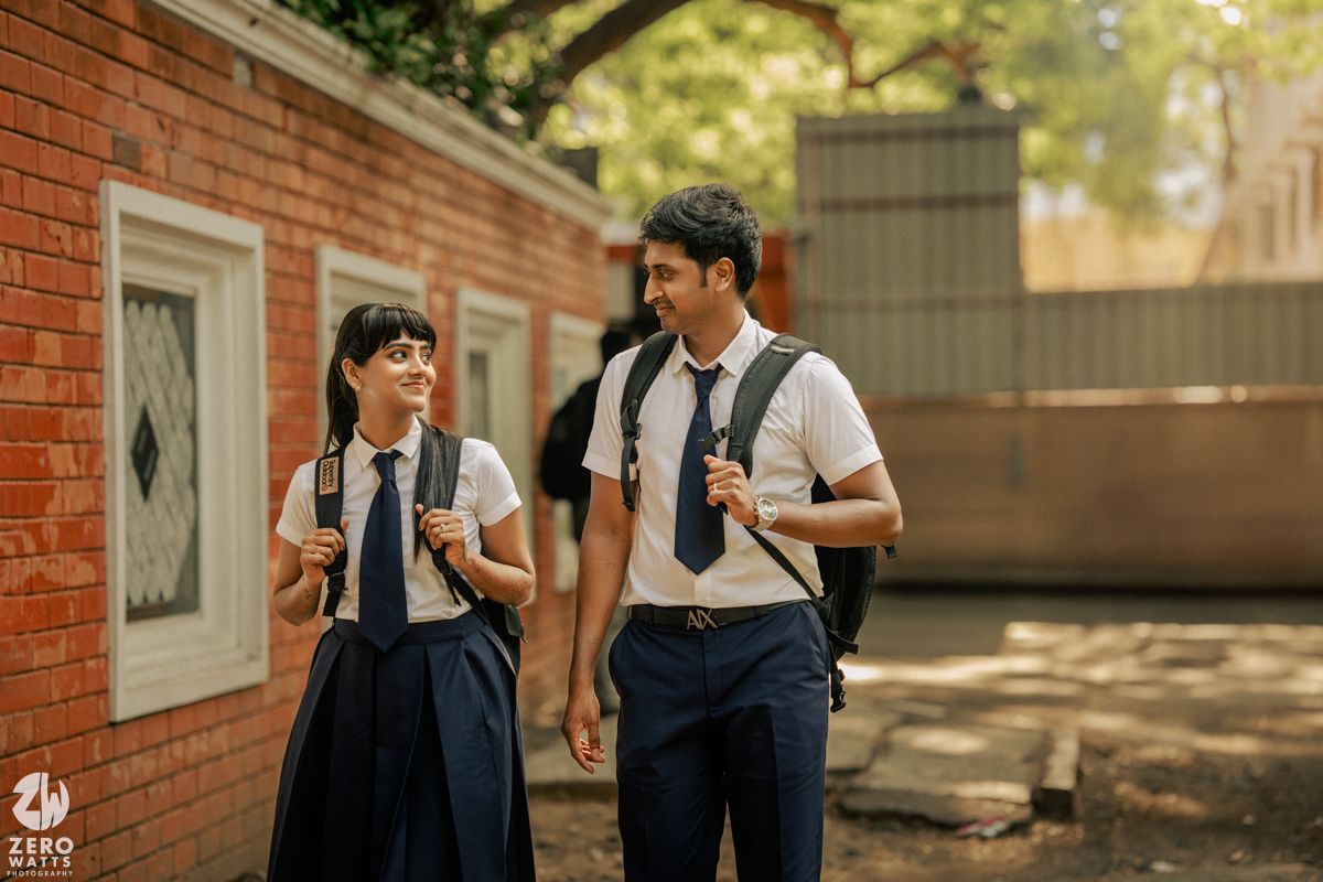 Students in uniforms socializing outside a brick building under sunlit trees.