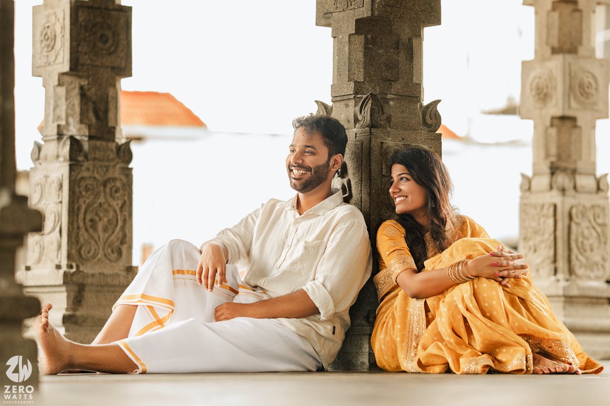 Couple in traditional Indian attire sharing romantic moments in a pillared stone corridor.
