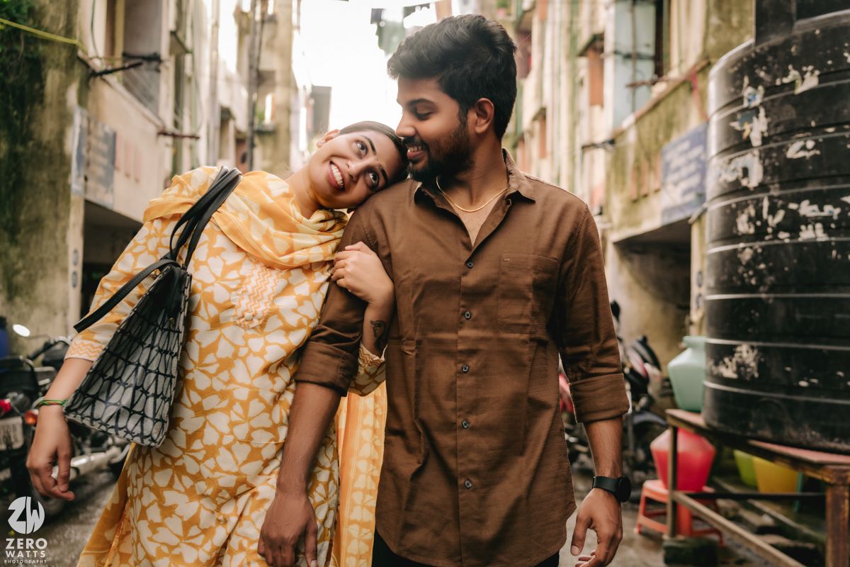 A couple in traditional attire poses romantically in an urban alleyway with vintage architecture and warm lighting.