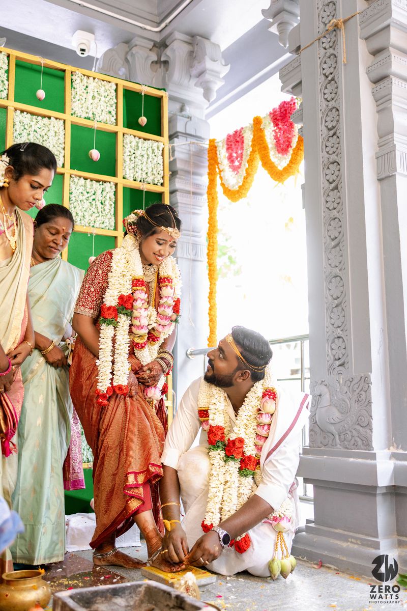 Traditional South Indian wedding ceremony taking place in an ornate temple hall decorated with marigold garlands and green panels.