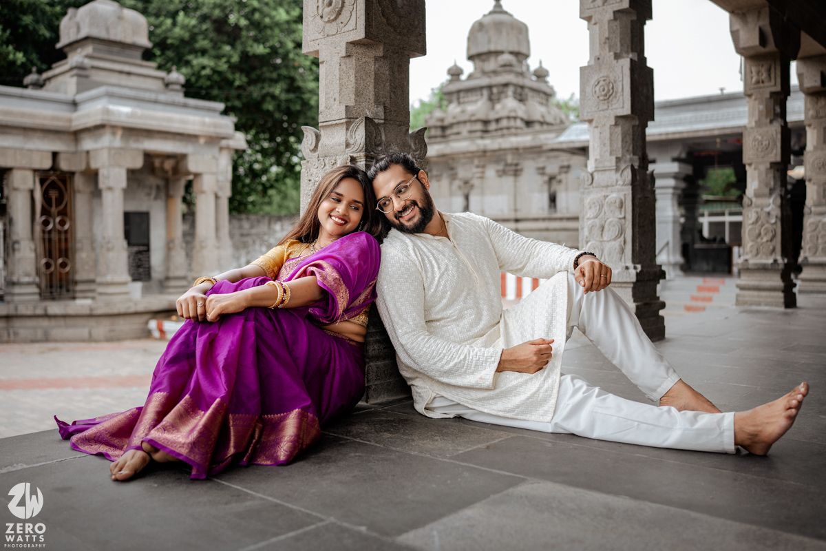 Couple in traditional Indian attire poses elegantly on ornate marble steps of a historic palace.