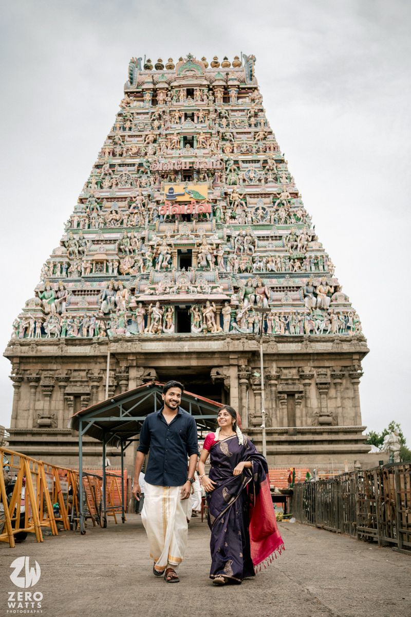 Couple poses in front of an ornate South Indian temple with traditional Dravidian architecture and carved gopuram.