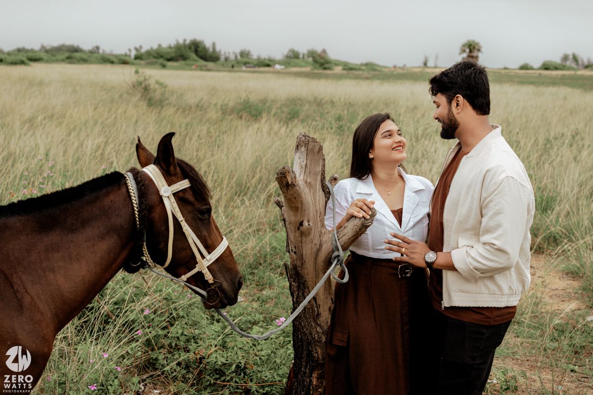 A romantic couple poses with horses in a rustic field setting during a countryside photoshoot.
