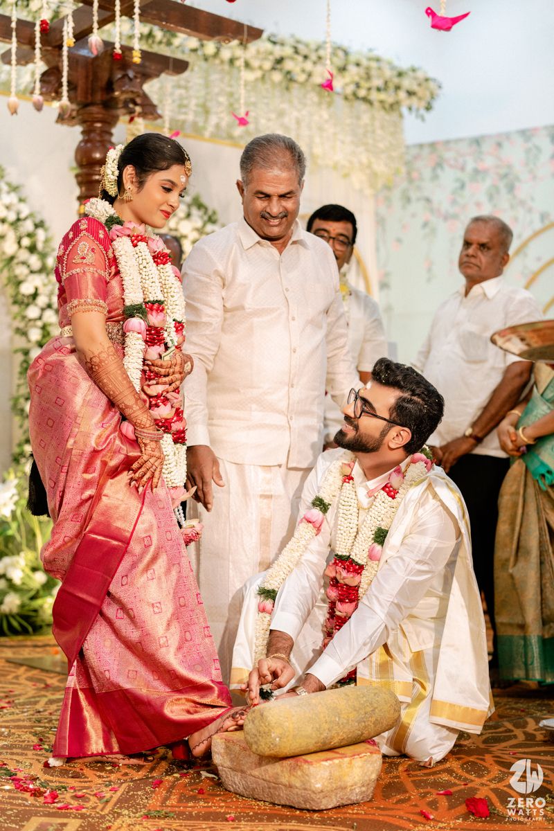 South Indian groom kneeling during Amavasai stone ritual with bride and family at wedding ceremony.
