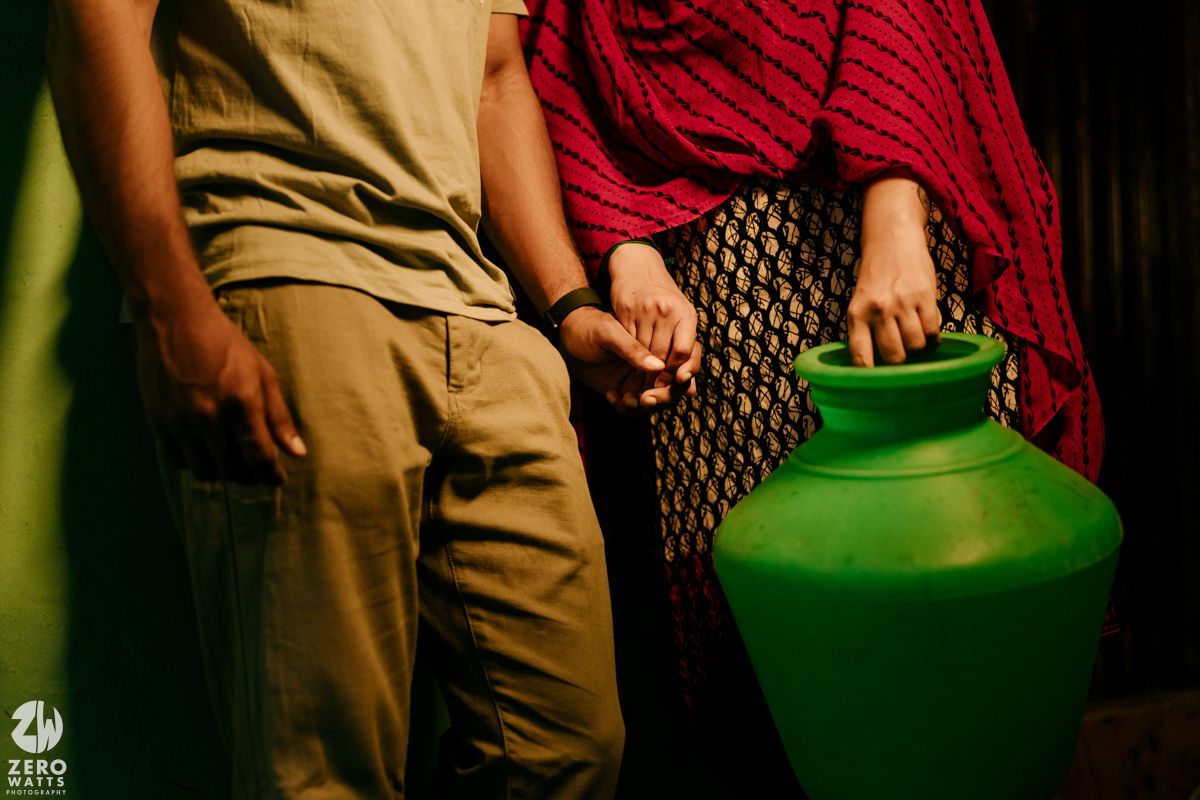 Person wearing tan pants and red shirt holds a bright green watering can against a dark background.