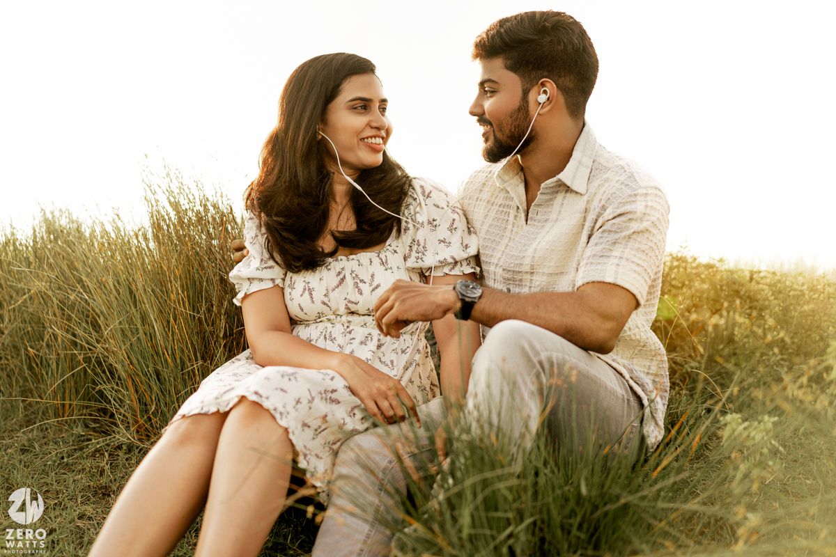 A couple sits together in tall grass during a romantic outdoor photoshoot at sunset.
