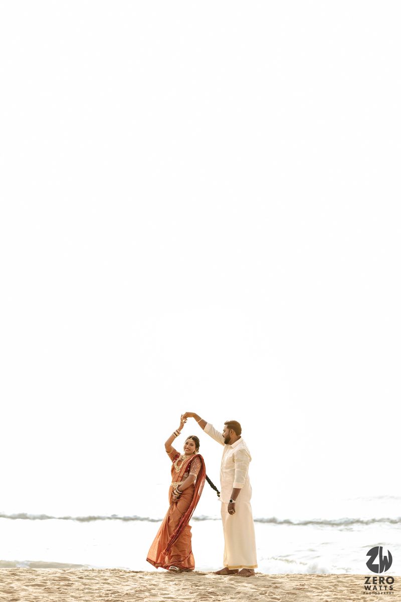Two people in flowing dresses dance together on a serene beach with ocean waves in the background.