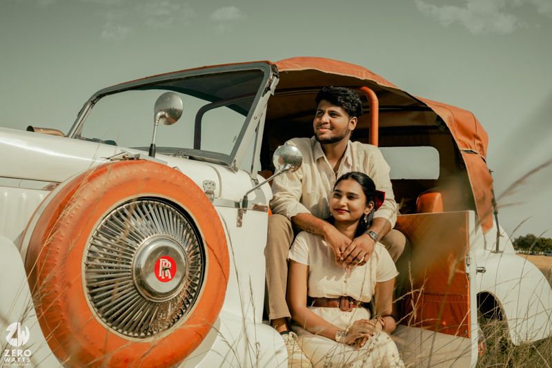 Vintage themed photo with couple in retro clothing posing in classic car with orange spare tire cover.