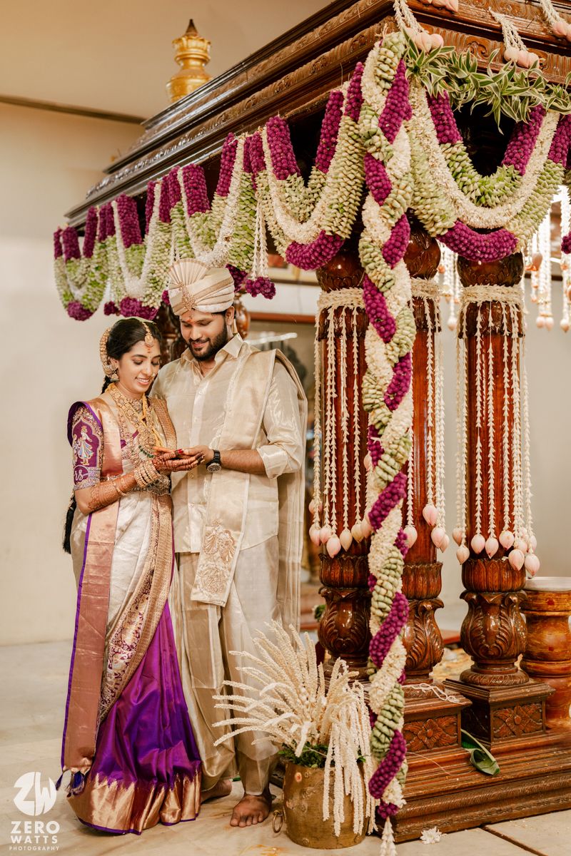 Couple sharing intimate moment under ornate mandap decorated with pink and white flower garlands at Indian wedding.