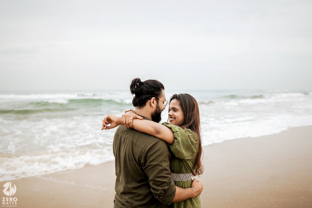 Two people share an intimate moment while standing on a sandy beach near the ocean.