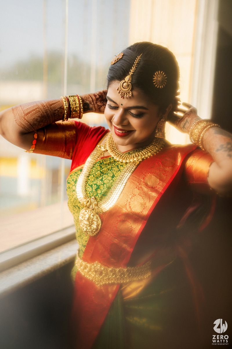 Smiling South Indian bride in green and red silk saree adorned with gold jewelry and traditional bridal makeup.