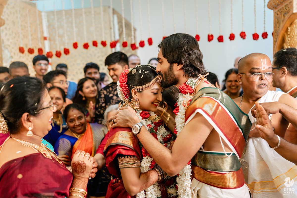 Bride and groom exchange garlands during a traditional South Indian Hindu wedding ceremony surrounded by family.