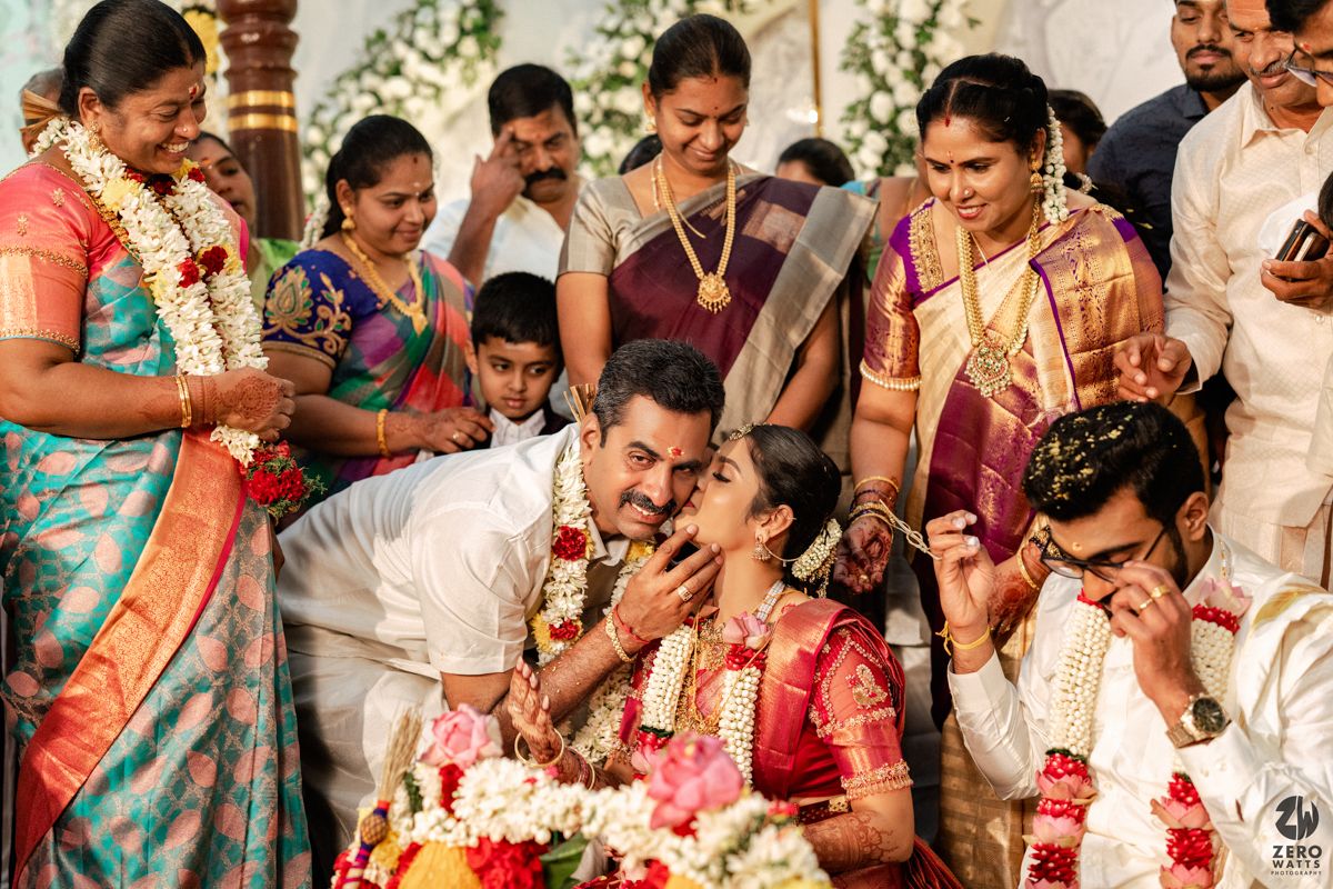 Colorful South Indian wedding ceremony with bride and groom exchanging garlands surrounded by family in traditional silk sarees.