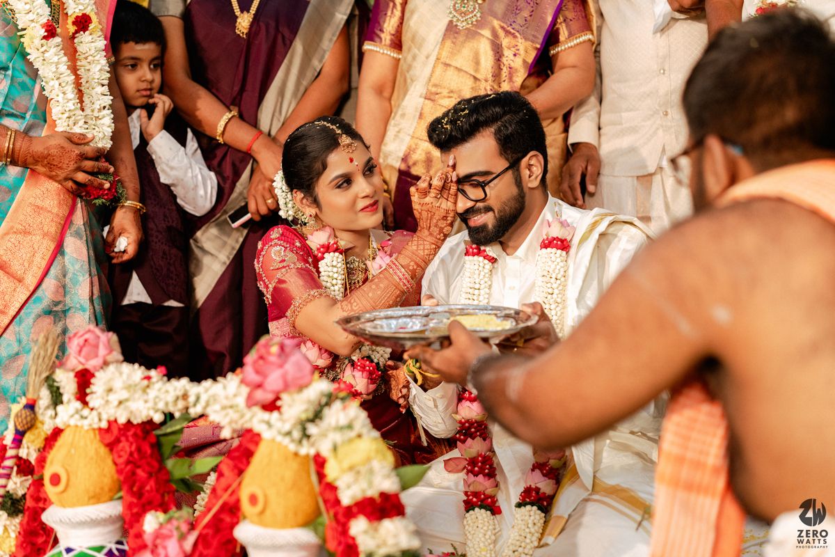 South Indian wedding ceremony couple performing traditional rituals with priest and guests in attendance.