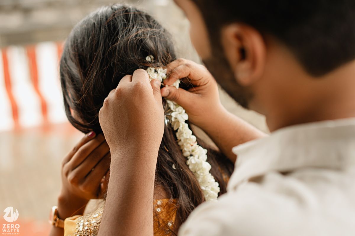 Someone gently places a delicate white jasmine flower garland in dark hair during a traditional ceremony.
