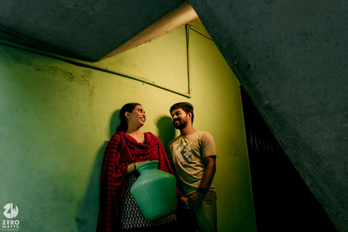A couple stands intimately together in dramatic lighting against a green wall.